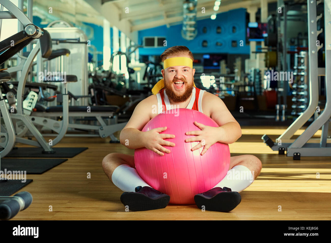 Funny fat man with a ball sitting on the floor smiling at the gy Stock Photo