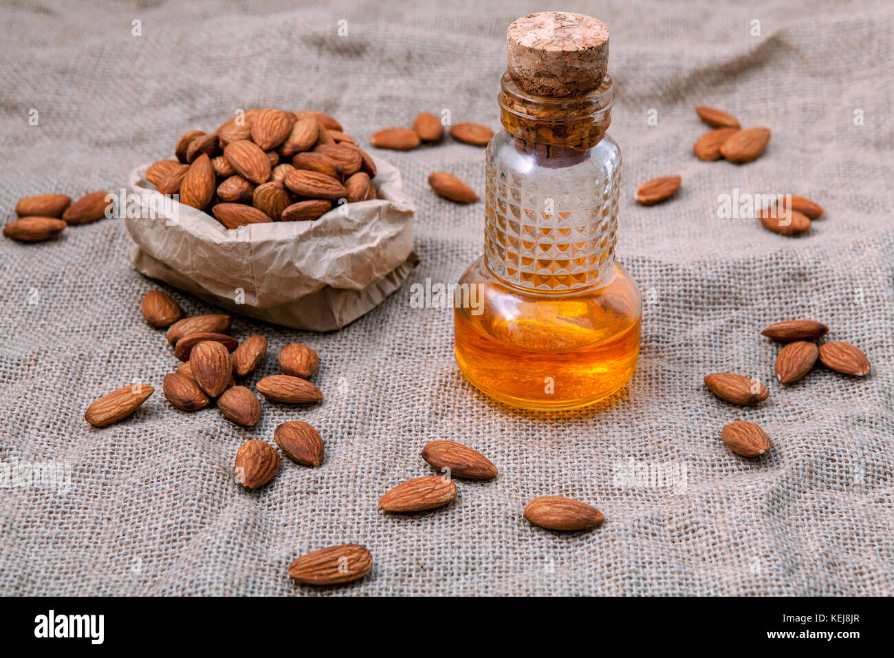 Bottle of extra virgin almonds oil with whole almonds on hempsack