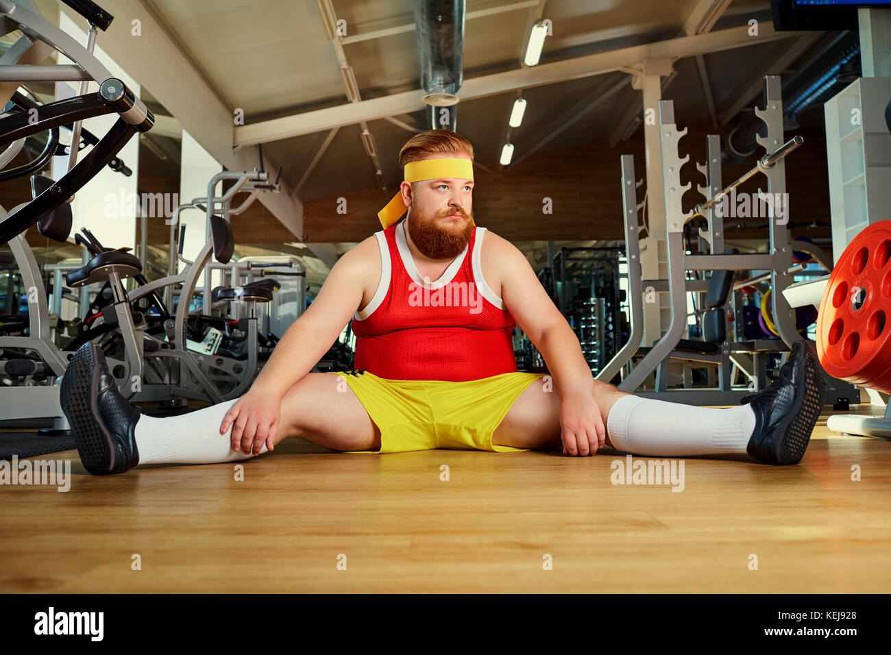Fat funny man tired sitting on the floor in the gym Stock Photo