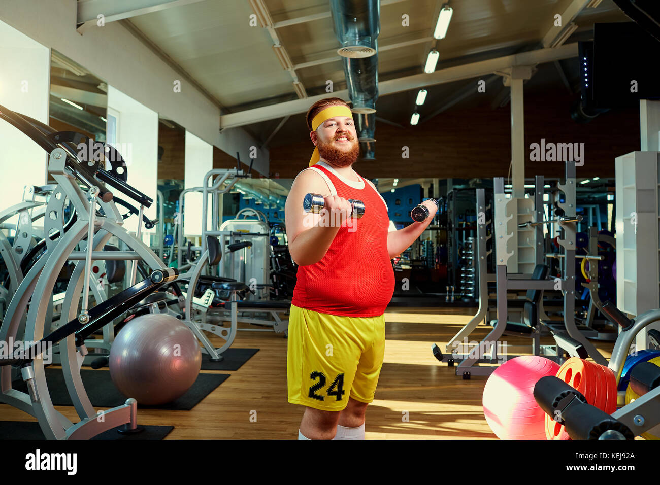 Fat funny man with dumbbells in the gym Stock Photo