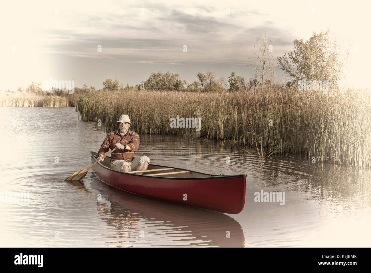 senior male paddler paddling a canoe on a calm lake, retro opalotype toning Stock Photo