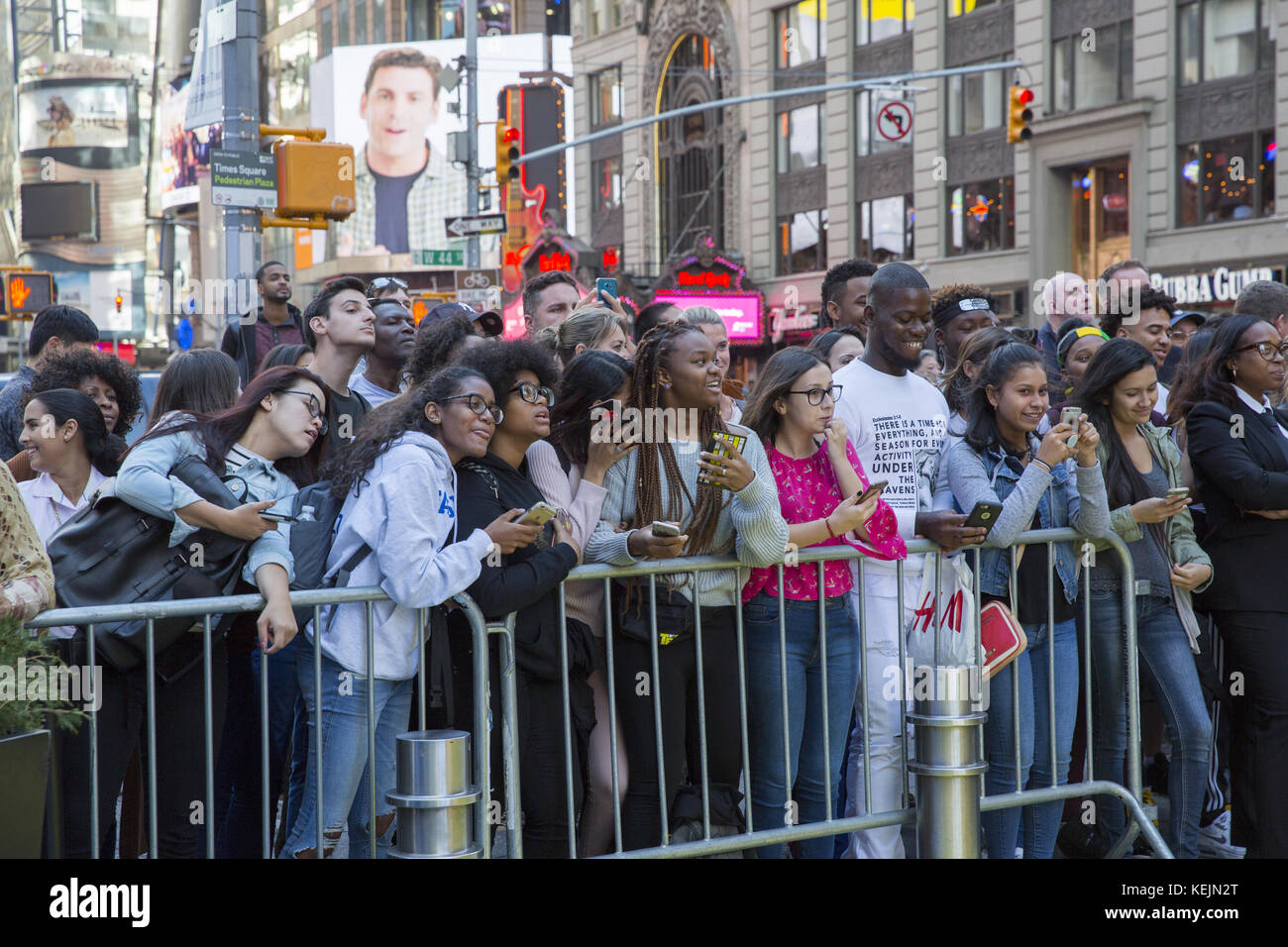 Young people & tourists stand behind barricades in Times Square to get a look at celebrity singers performing on the outdoor stage there. New York City. Stock Photo