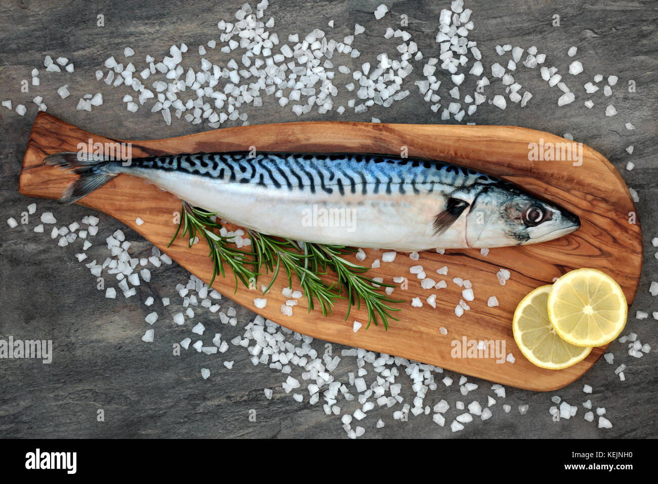 Mackerel fish health food on an olive wood board with course salt, rosemary herb and lemon fruit on marble background. High in omega 3 . Stock Photo