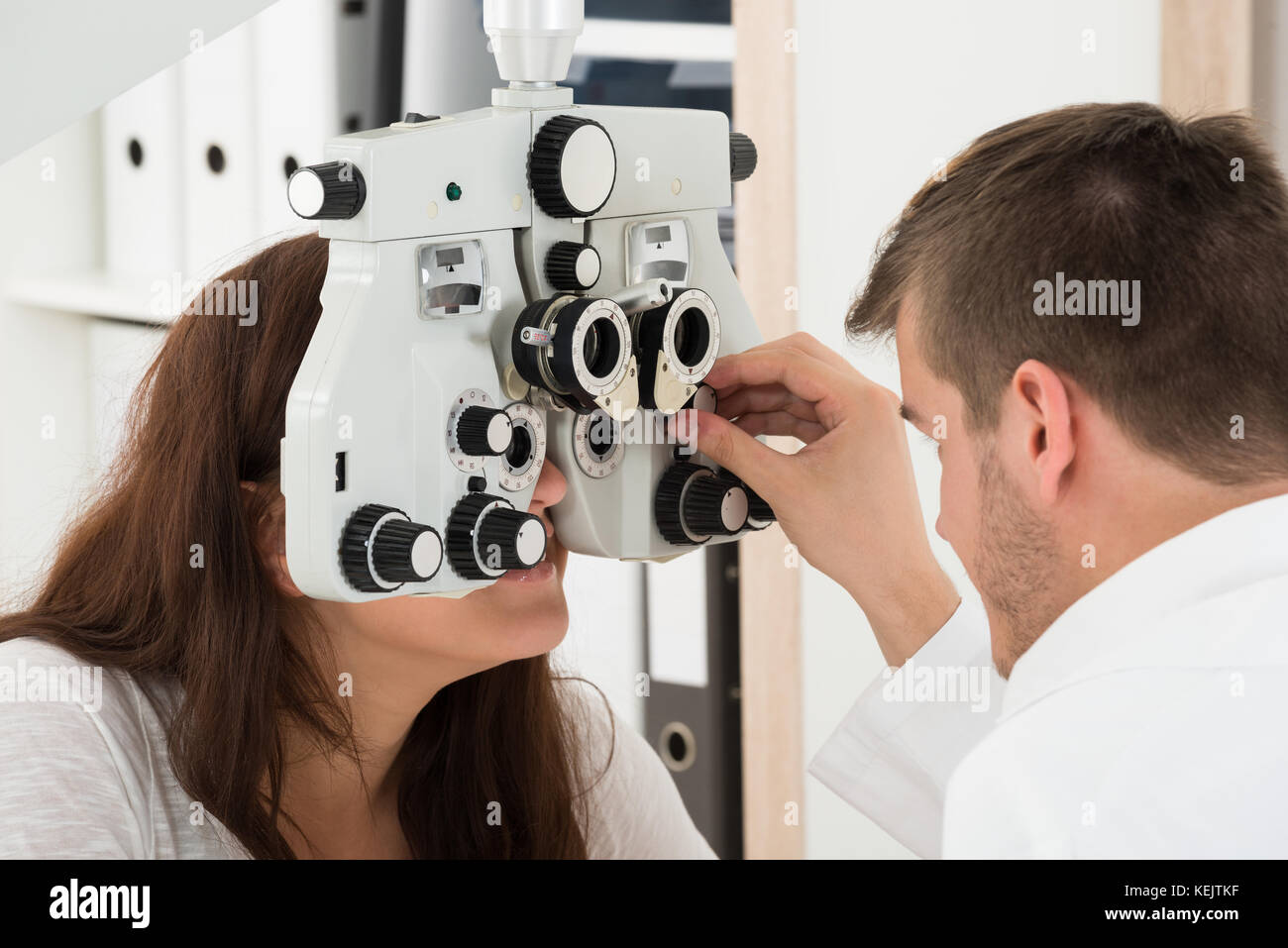 A Male Ophthalmologist Adjusting The Panel Of Phoropter While Examining Female Patient's Eyes Stock Photo