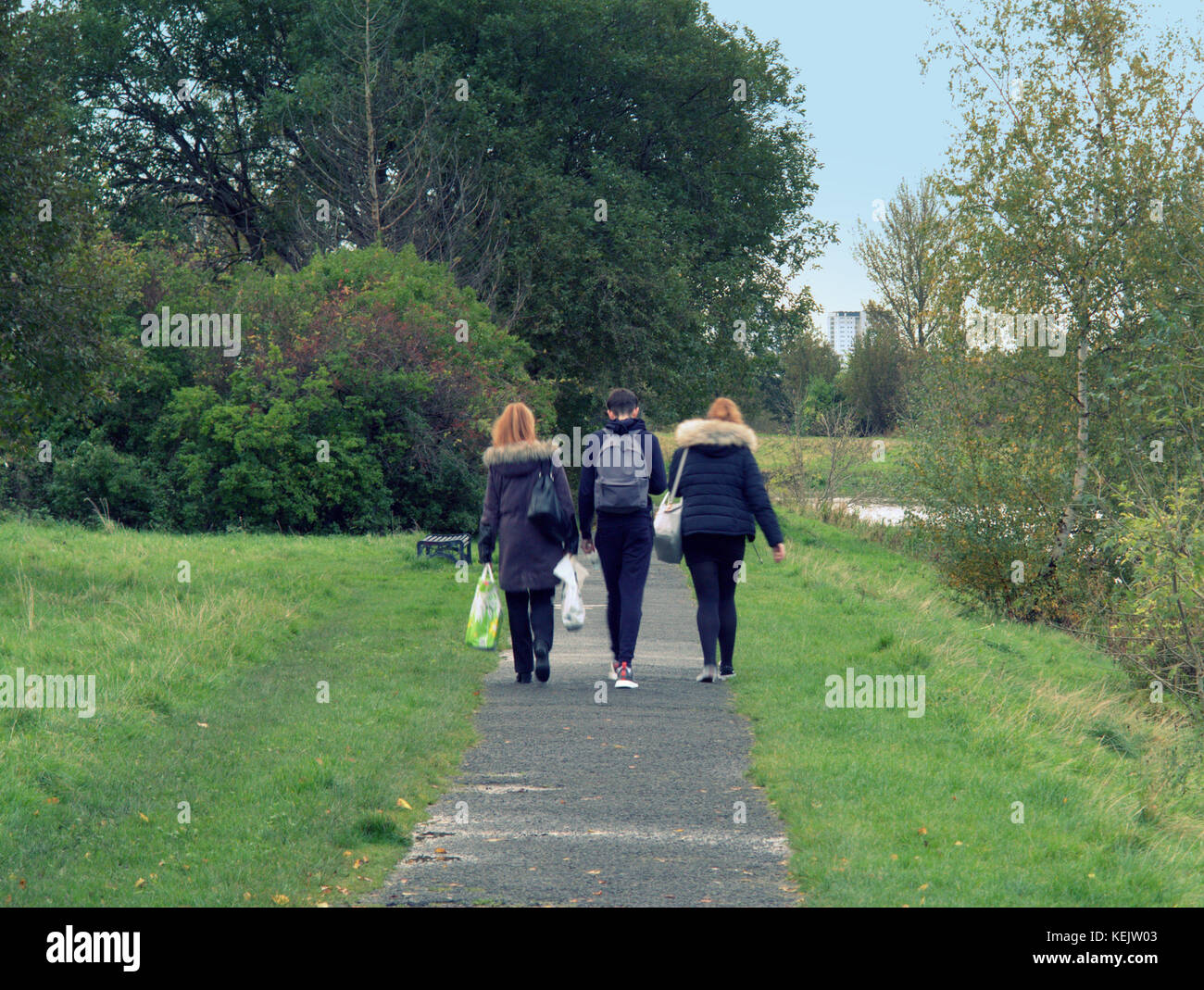 three young students boys and girls  backpacks walking viewed from behind on forth and clyde canal towpath  sidewalk pavement Stock Photo