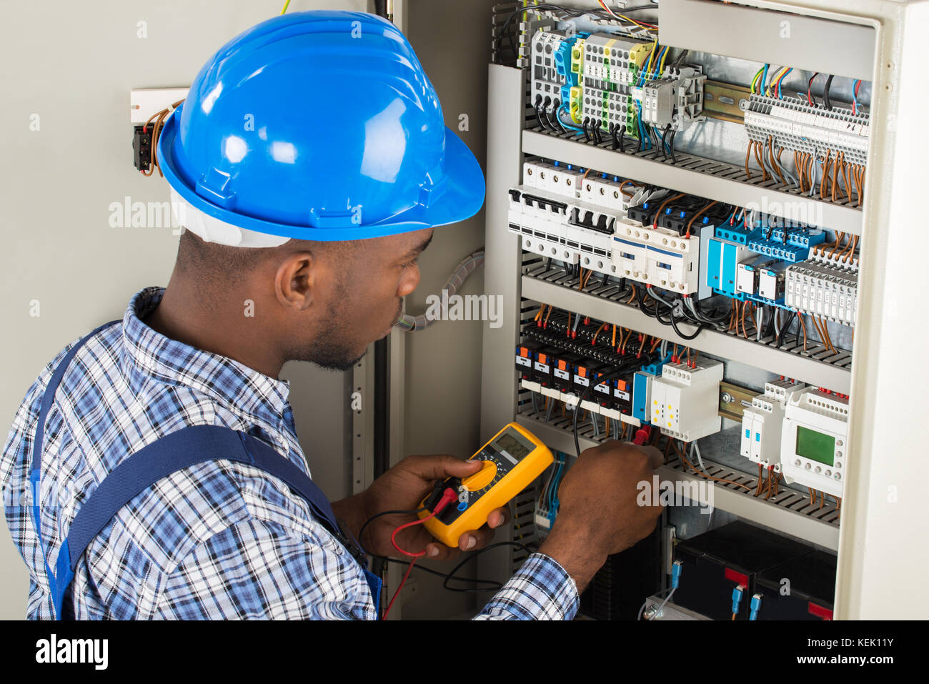 Young African Male Technician Examining Fusebox With Multimeter Probe Stock Photo