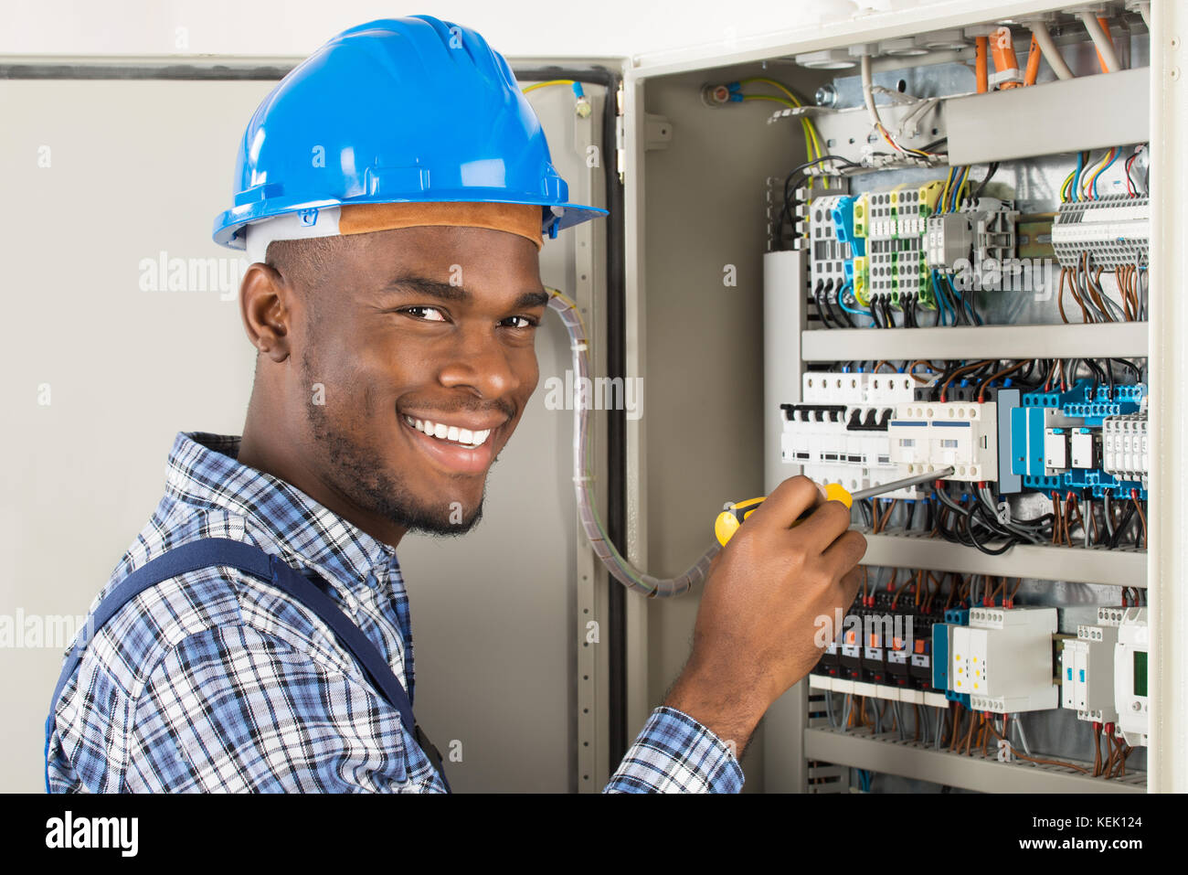 Portrait Of Happy African Male Technician Checking Fusebox With Screwdriver Stock Photo
