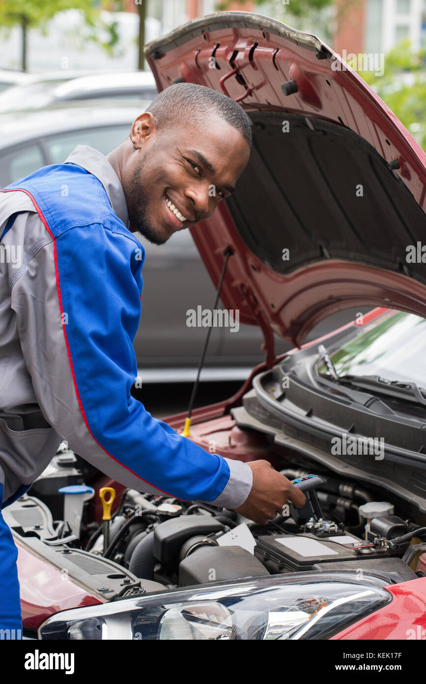 Young Happy Male Mechanic Testing Car Battery With Multimeter Stock Photo