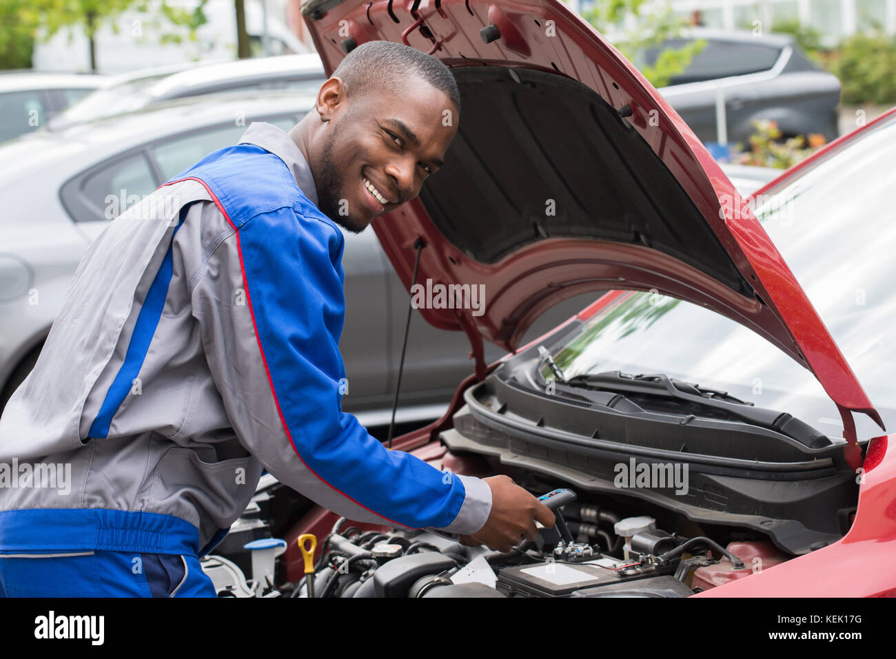Young Happy Male Mechanic Testing Car Battery With Multimeter Stock Photo