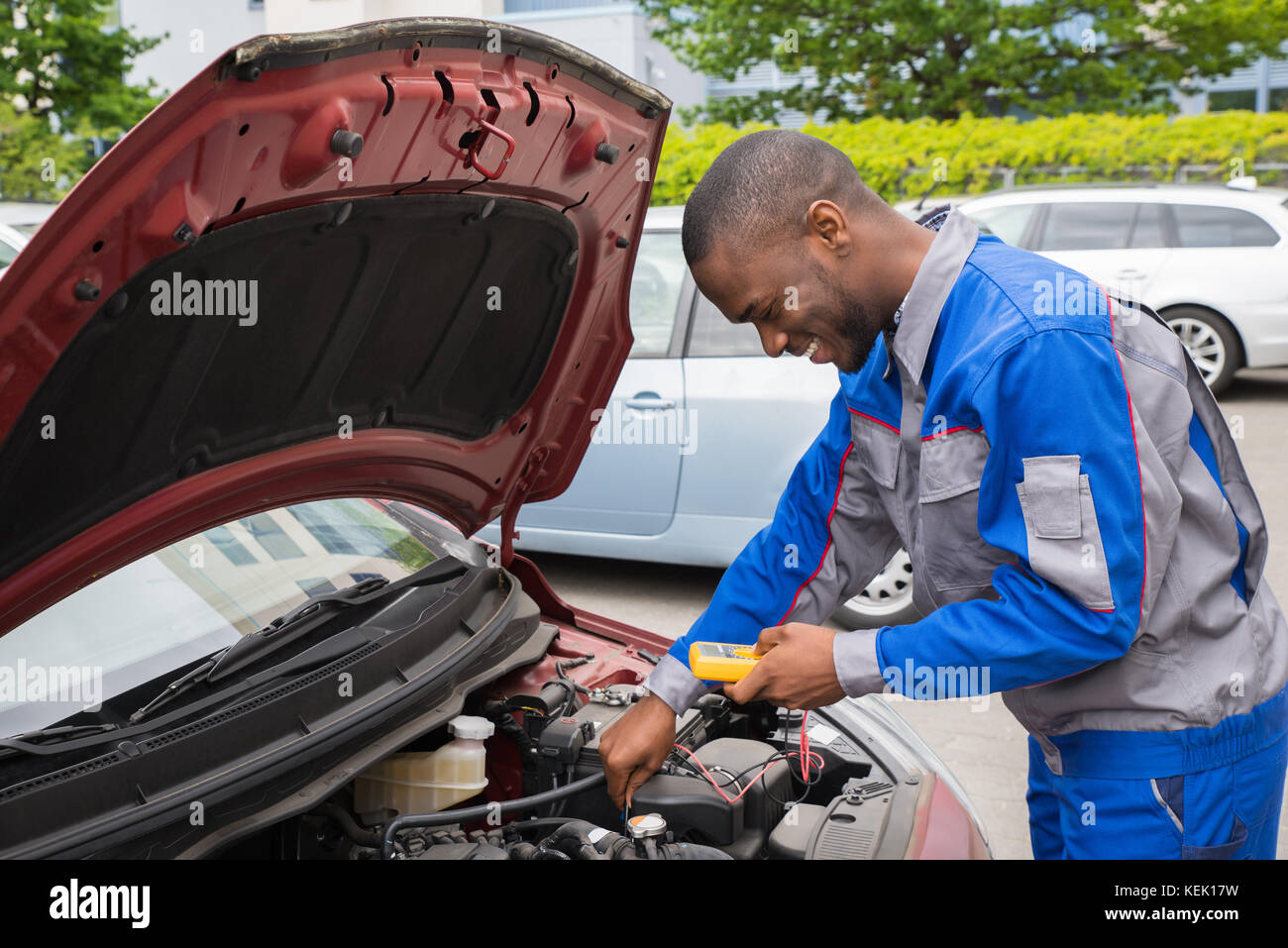 Happy Mechanic Using Multimeter To Check The Voltage Level In A Car Battery Stock Photo