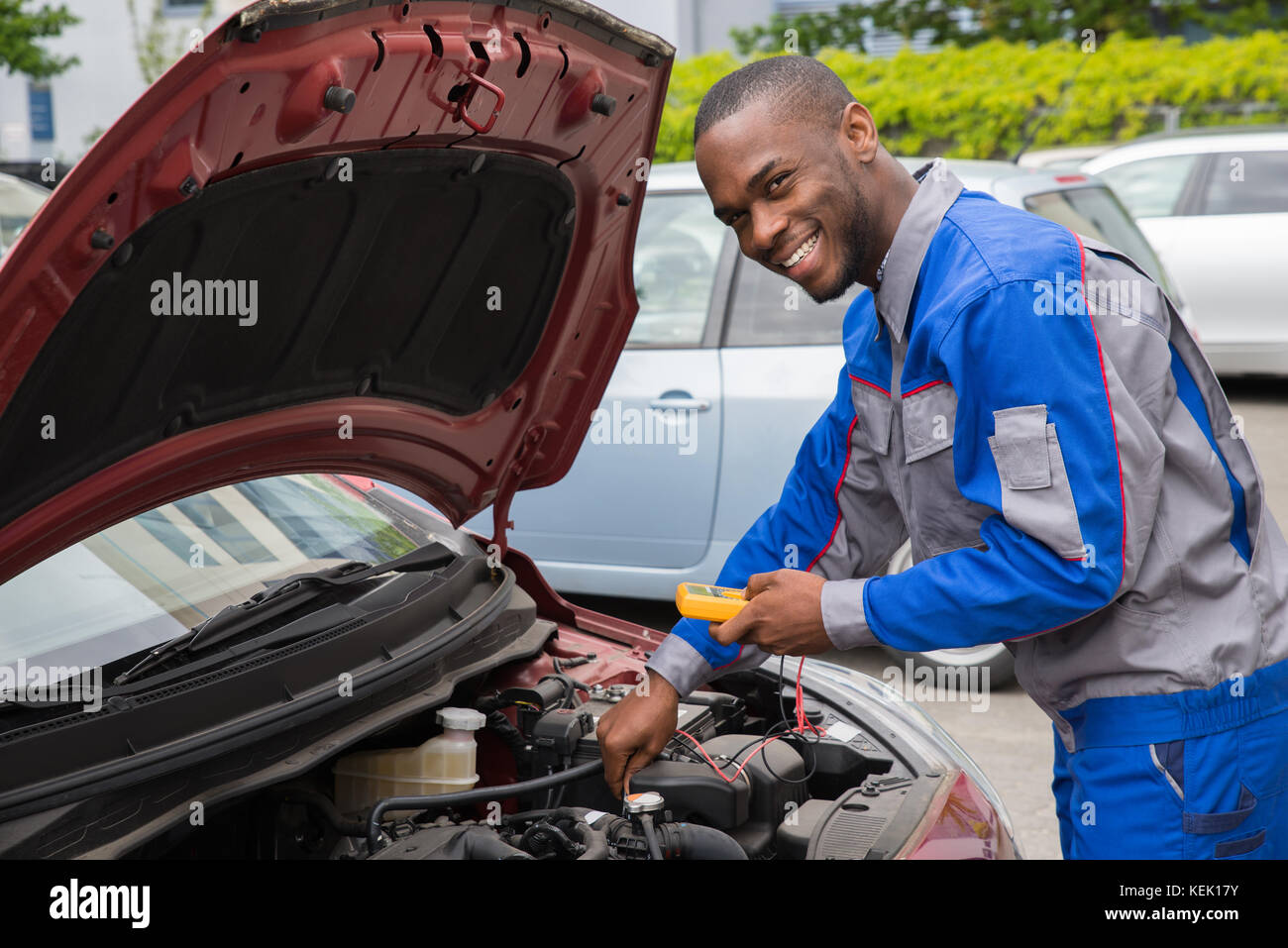 Happy Mechanic Using Multimeter To Check The Voltage Level In A Car Battery Stock Photo