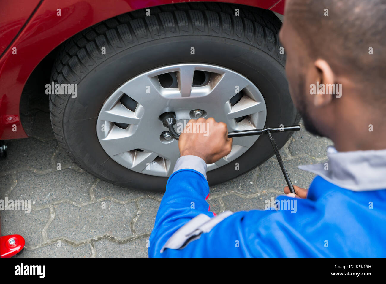 Young African Mechanic Changing Tire Of A Red Car With Wrench Stock Photo