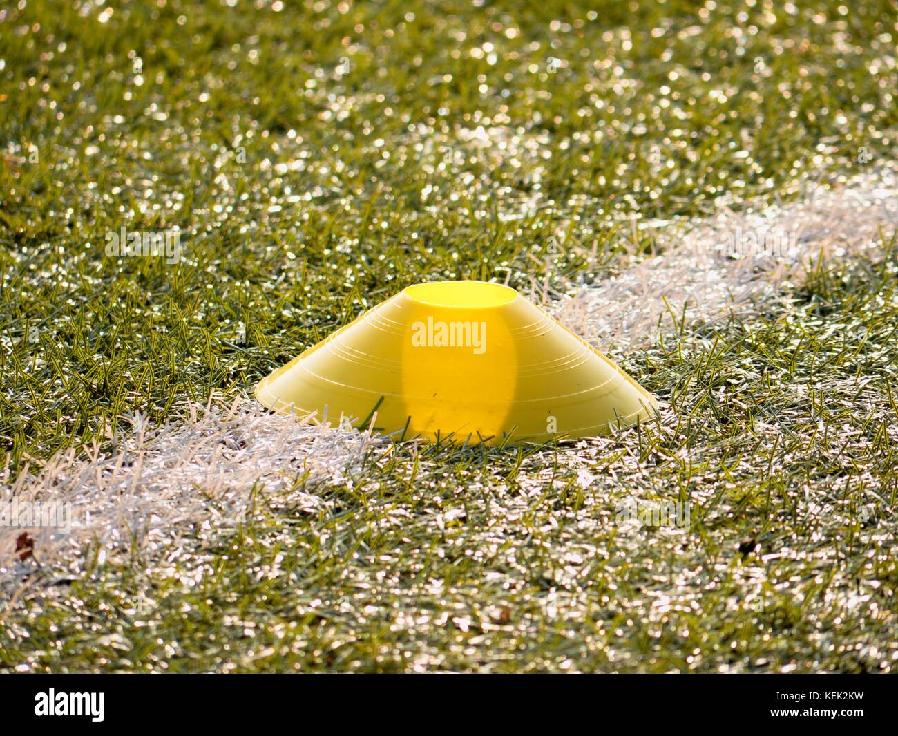 Bright yellow plastic cone on white soccer line. Plastic football green turf playground with