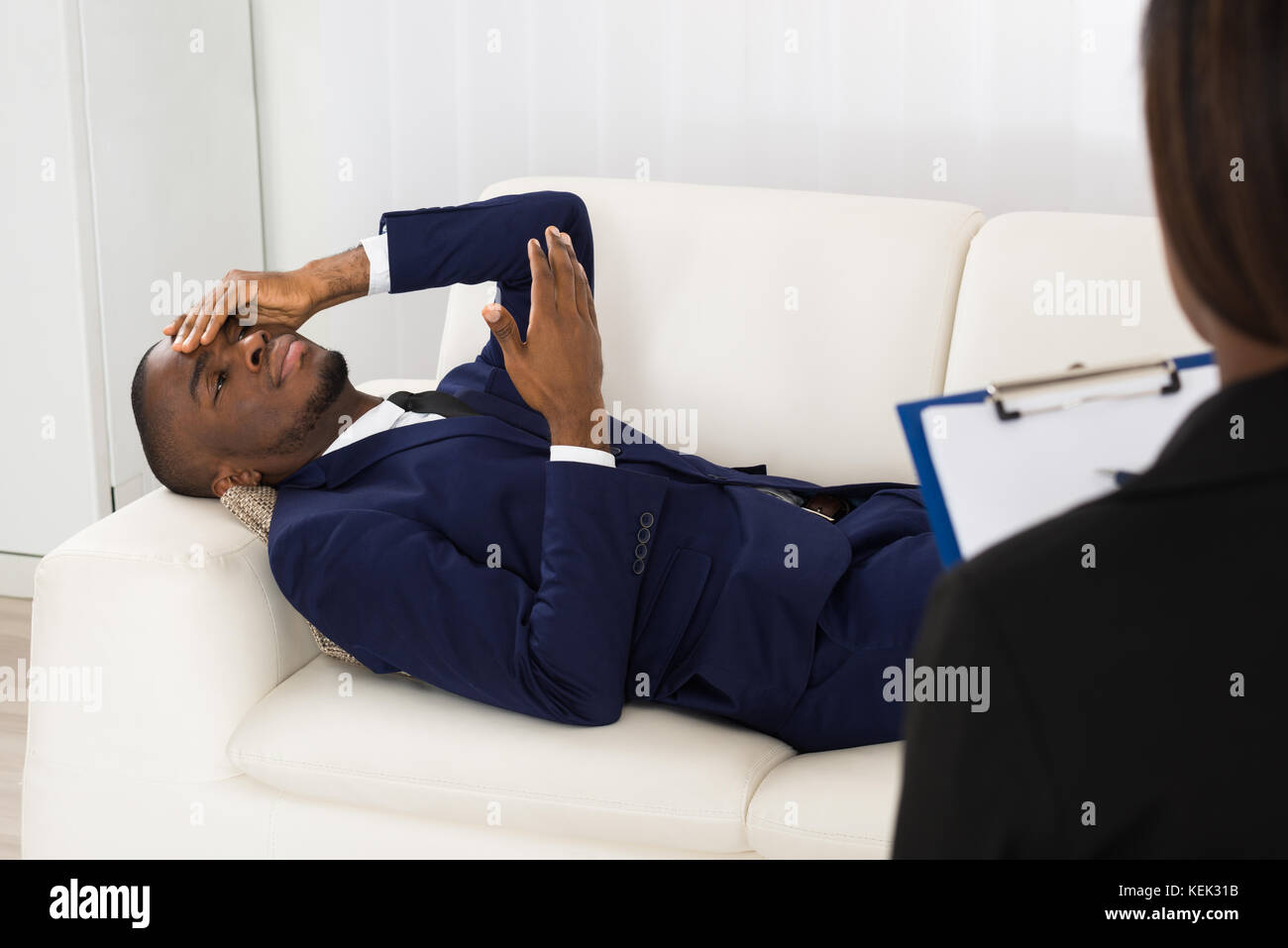 African American Man Laying On Couch In Front Of Psychiatrist With Clipboard Stock Photo