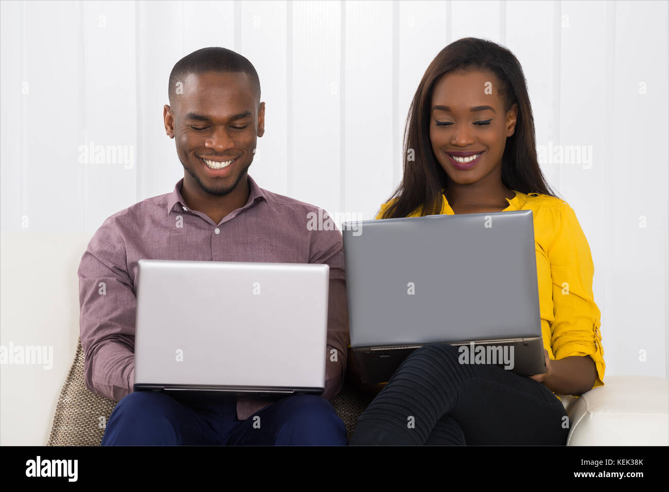Happy Young Couple Using Laptops While Sitting On Sofa Stock Photo - Alamy