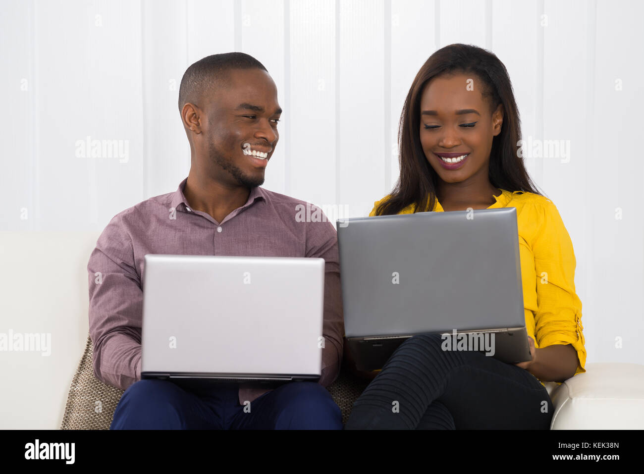 Happy Young Couple Using Laptops While Sitting On Sofa Stock Photo - Alamy