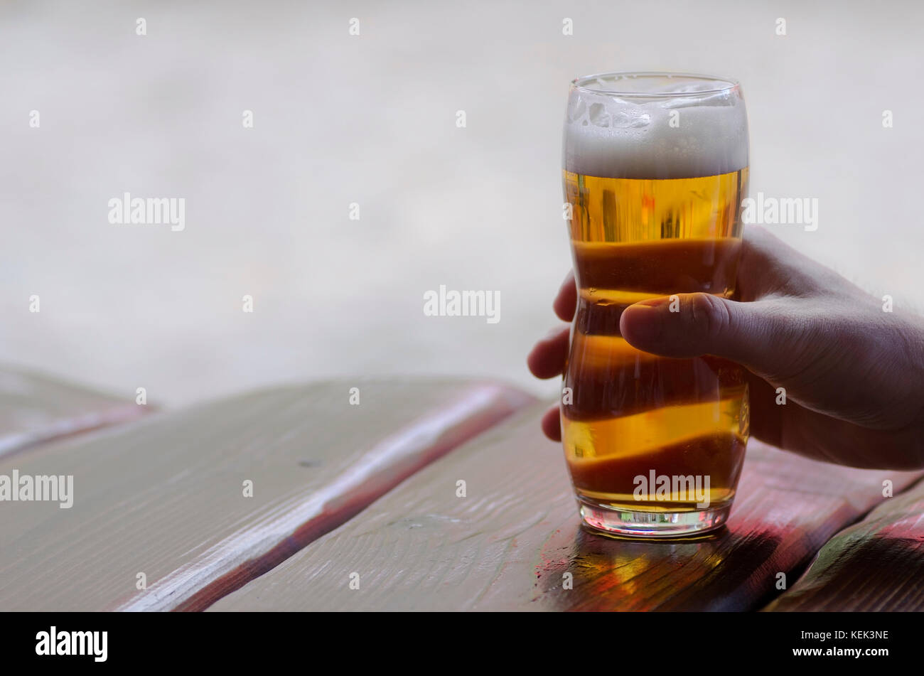 Close-up view of a hand holding a glass of beer lying on a table in a pub Stock Photo