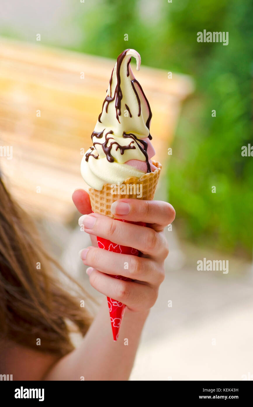 Close-up view of girl's hand holding ice cream with chocolate toping in wafer with blurred background Stock Photo