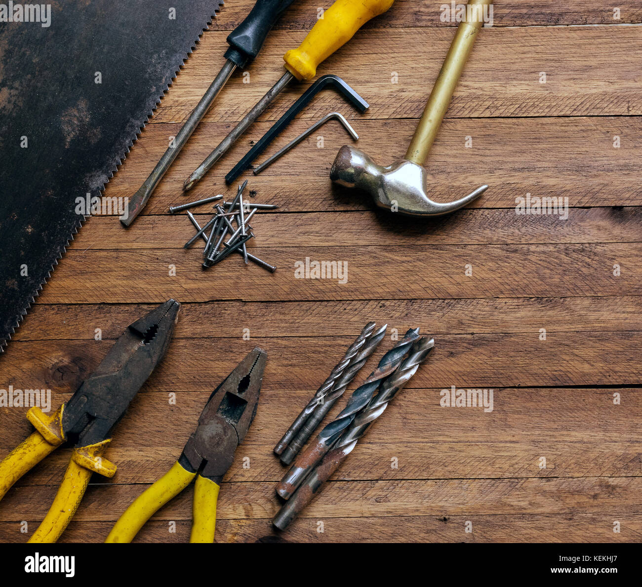 Rusty and old used carpentry and garage tools on a light brown wood background, showing varied tools,with metal pliers and saw,metal drill bits,hammer Stock Photo
