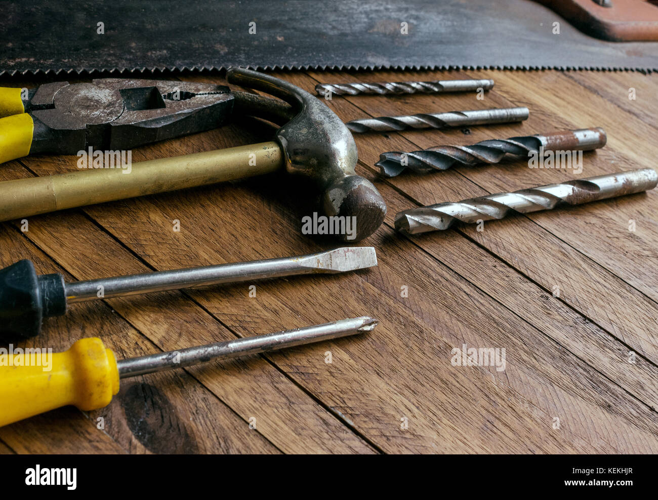 Rusty and old used carpentry and garage tools on a light brown wood background, showing varied tools,with metal pliers and saw,metal drill bits,hammer Stock Photo