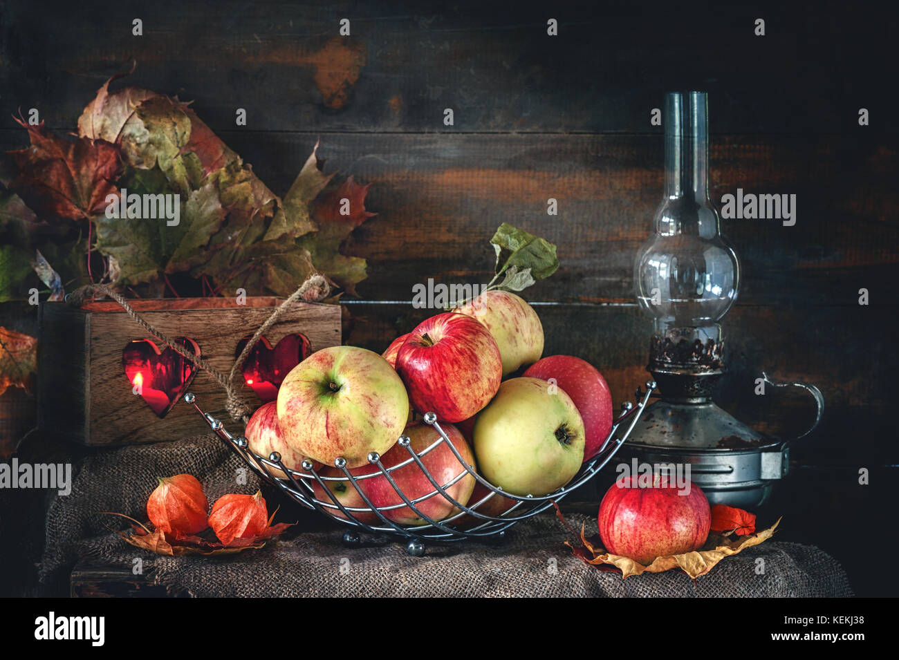 Autumn still life of apples in a basket with a lamp and candles. The ...