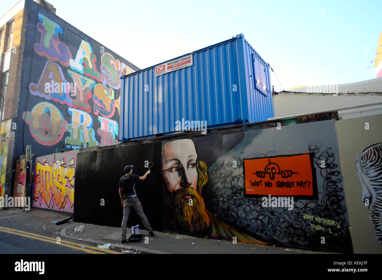 man using black paint & roller to paint over graffiti wall art in London, England Stock Photo