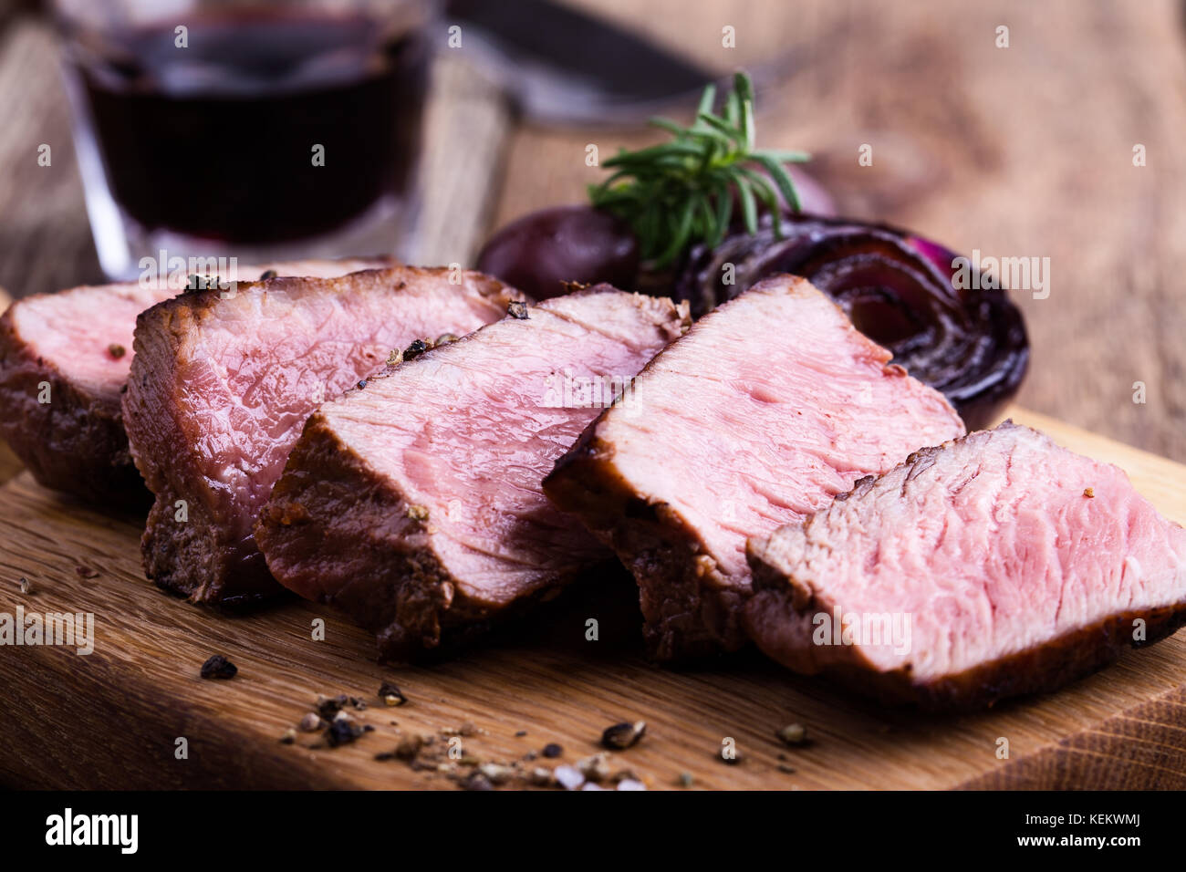 Delicious beef filet mignon served on wooden cutting board with roasted red onion and rosemary Stock Photo