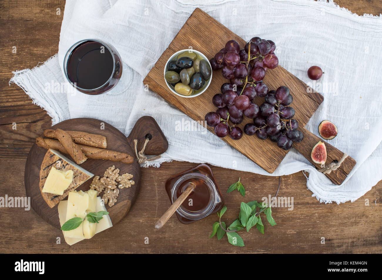 Glass of red wine, cheese board, grapes, walnuts, olives, honey and