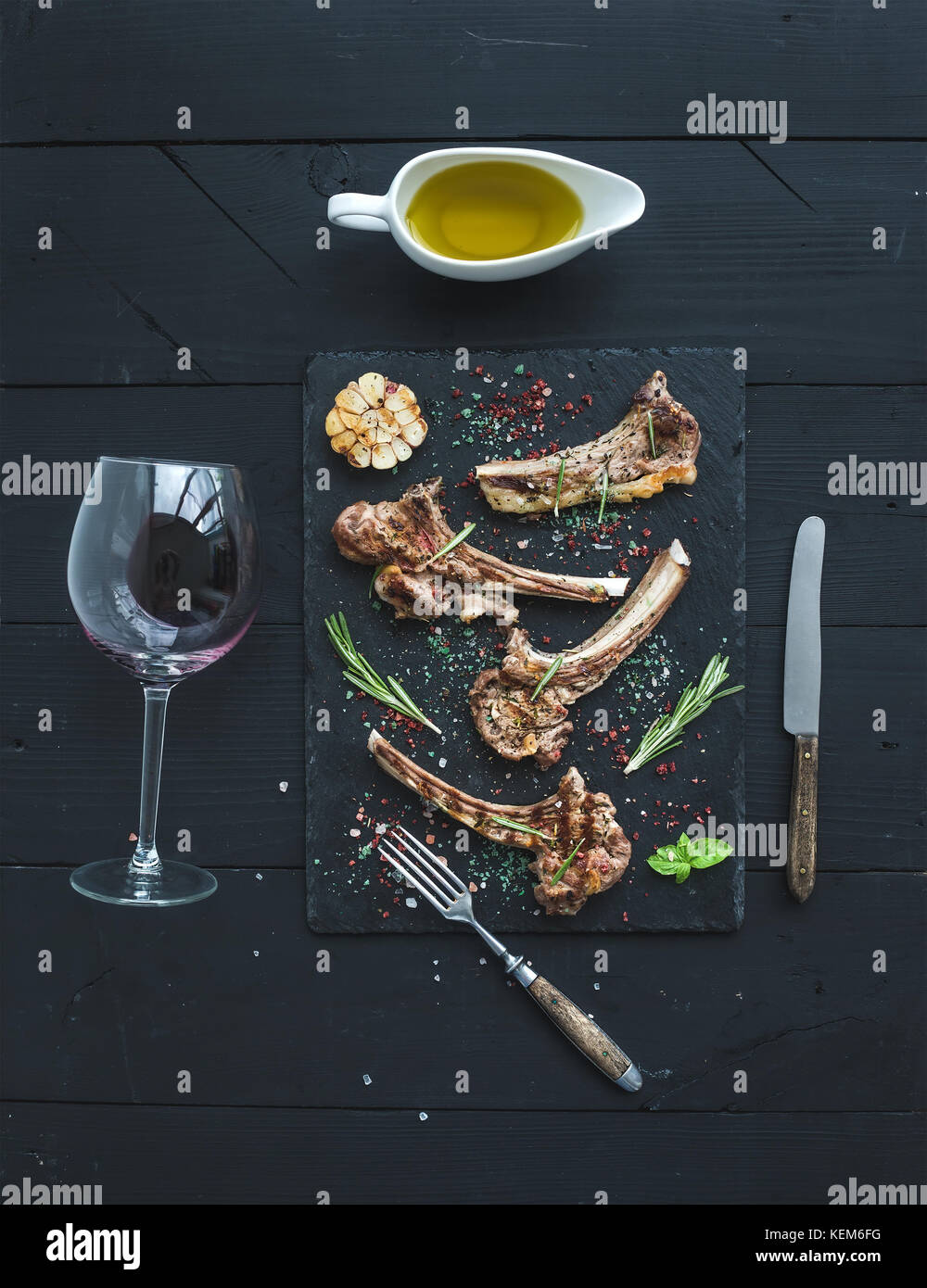 Grilled lamb chops. Rack of Lamb with garlic, rosemary, spices on slate tray, wine glass, oil in
