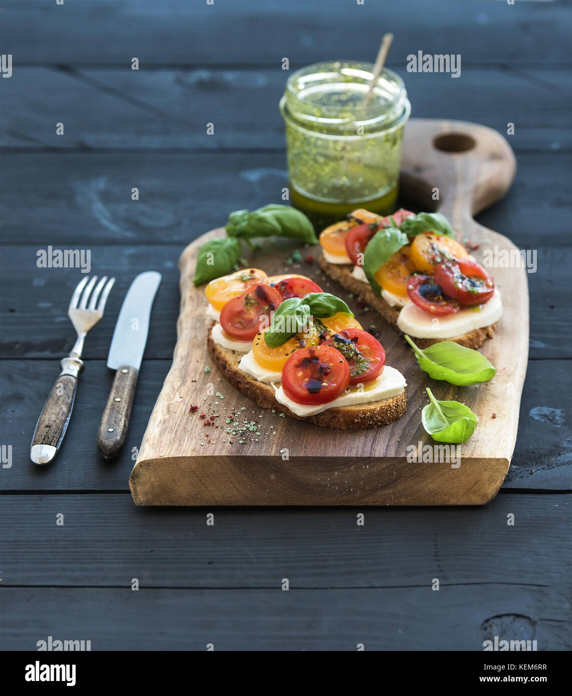 Tomato, mozzarella and basil sandwiches on dark wooden chopping board