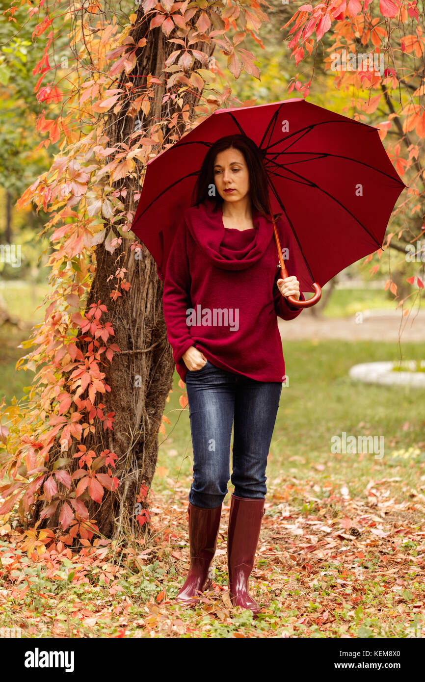 Young woman (brunette) in jeans, a sweater and crimson rubber boots is  walking in an autumn park. Selective focus Stock Photo - Alamy