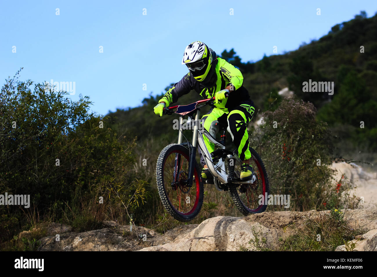 Downhill mountain biker on a yellow costume making a small jump Stock Photo