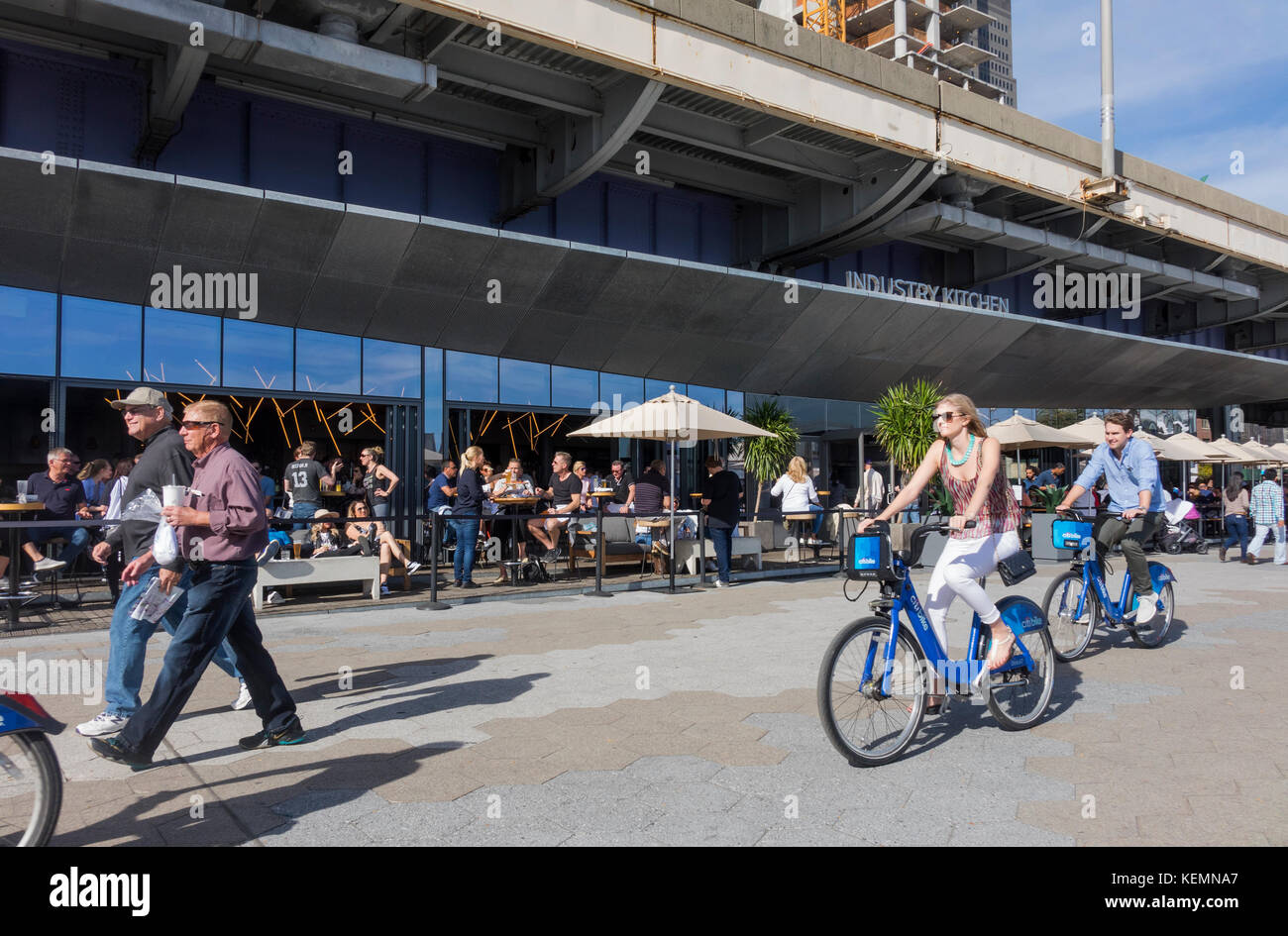 People walking and biking past the Industry Kitchen, a restaurant on the East River near Wall Street Stock Photo