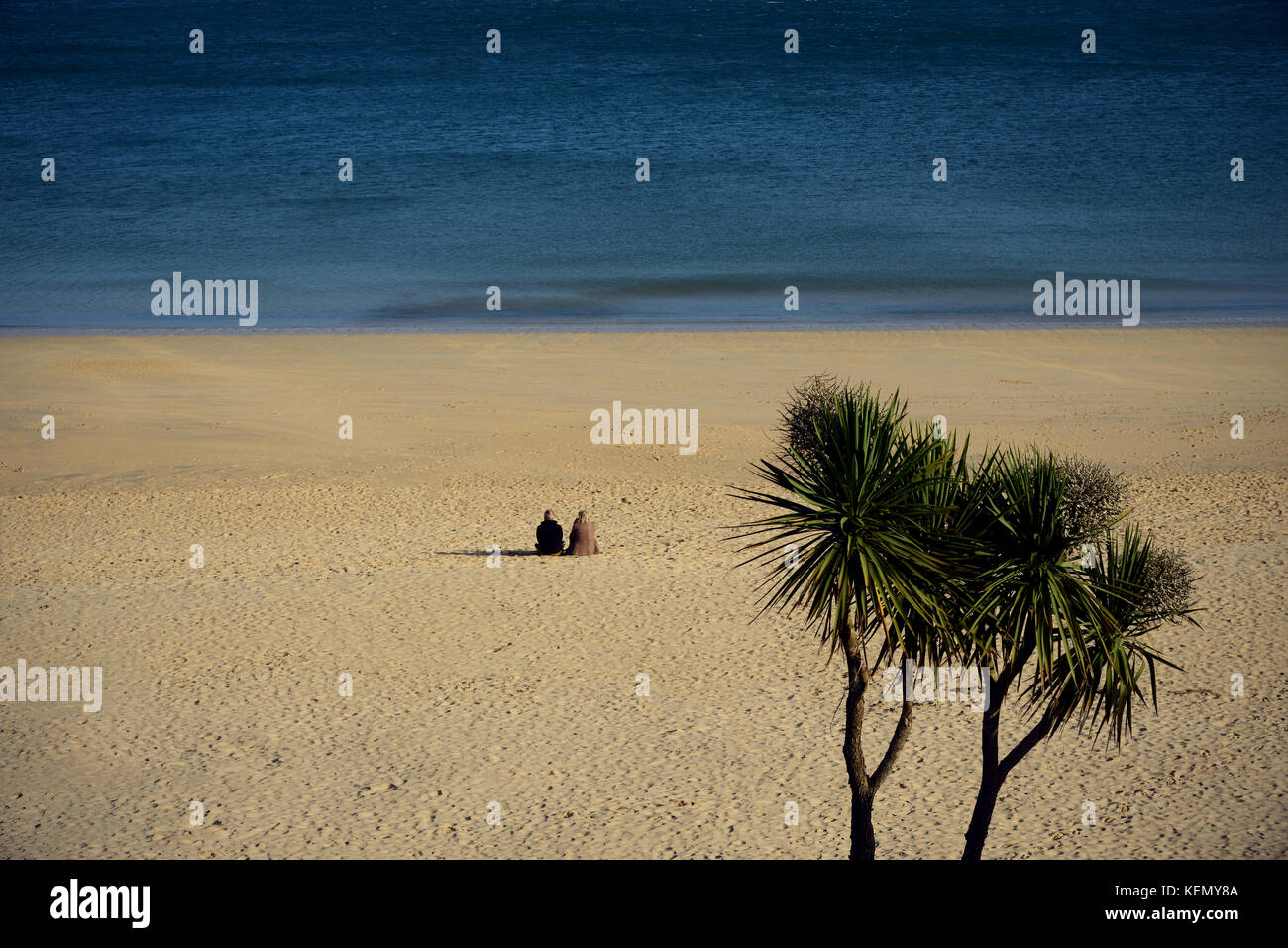 A couple relax in the tranquil surroundings of sand and sea at Carbis Bay near St Ives, Cornwall Stock Photo