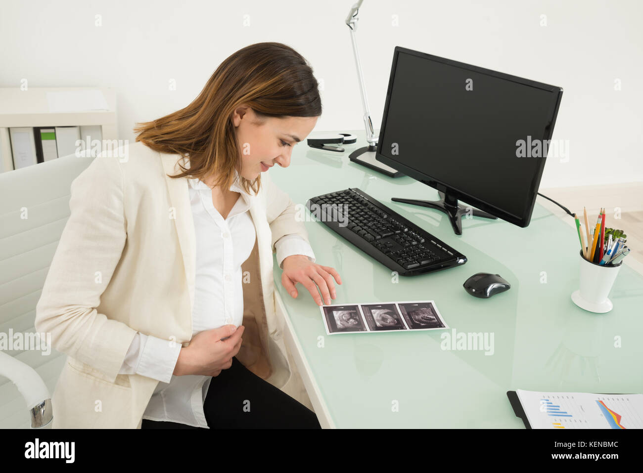 Happy Pregnant Businesswoman Looking At Ultrasound Scan Report On Desk Stock Photo