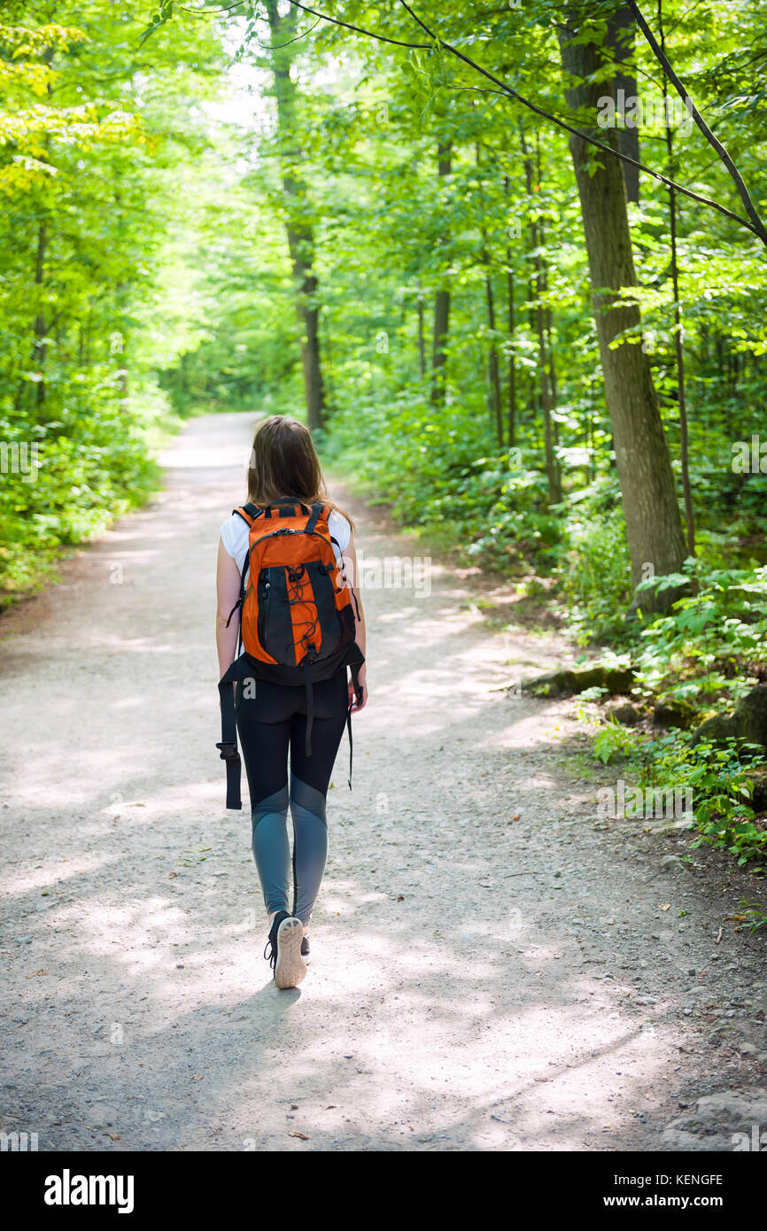 Young woman hiker with backpack walking on hiking trail in sunny summer forest. Hilton Falls conservation area, Ontario, Canada. Stock Photo