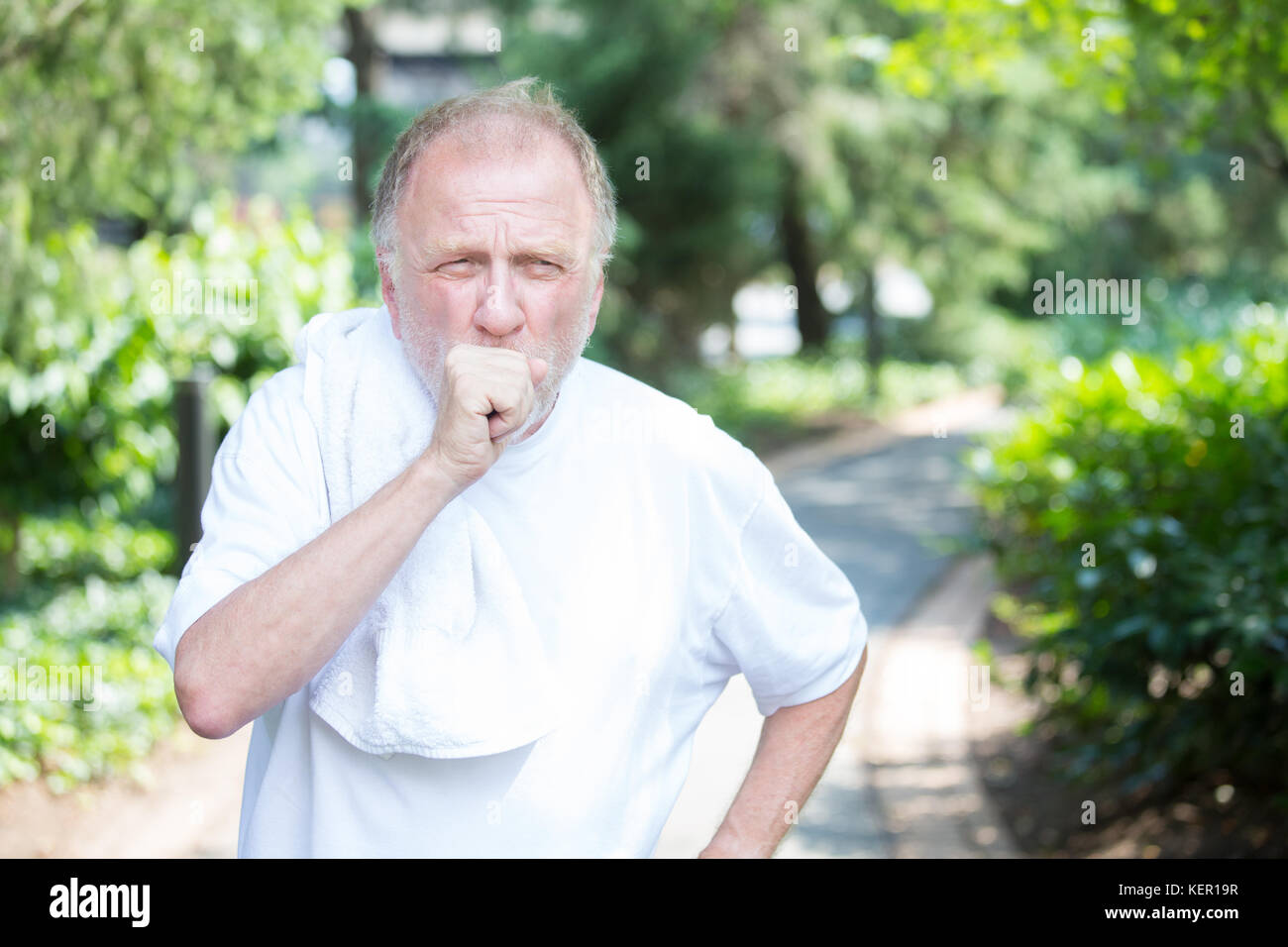 Closeup portrait, senior guy holding towel, very tired, exhausted from over exertion, coughing catching breath, isolated outdoors outside green trees  Stock Photo