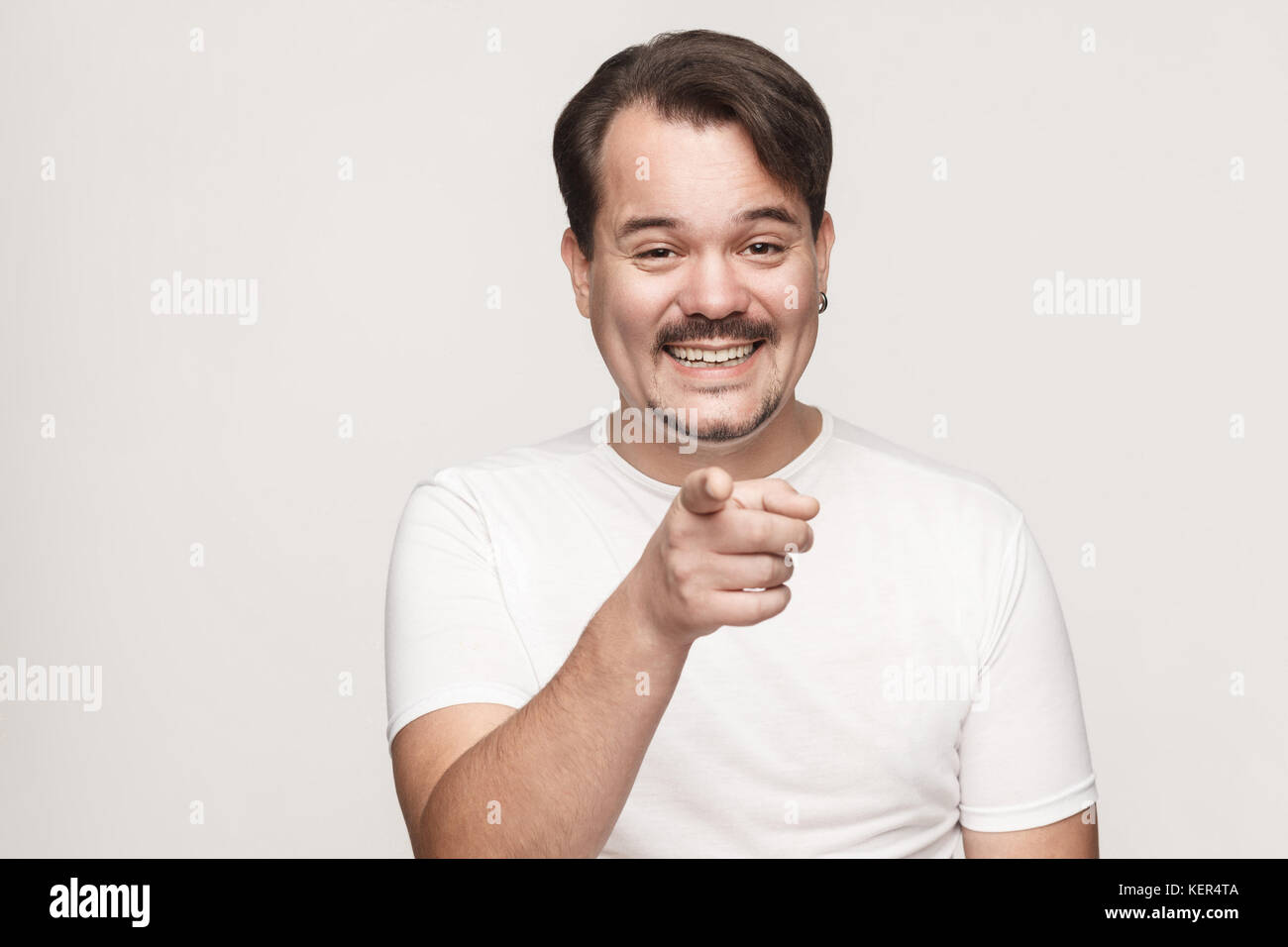 The happiness man, wearing white tshirt, having happiness looks, pointing finger at camera and toothy smiling. Isolated studio shot on gray background Stock Photo