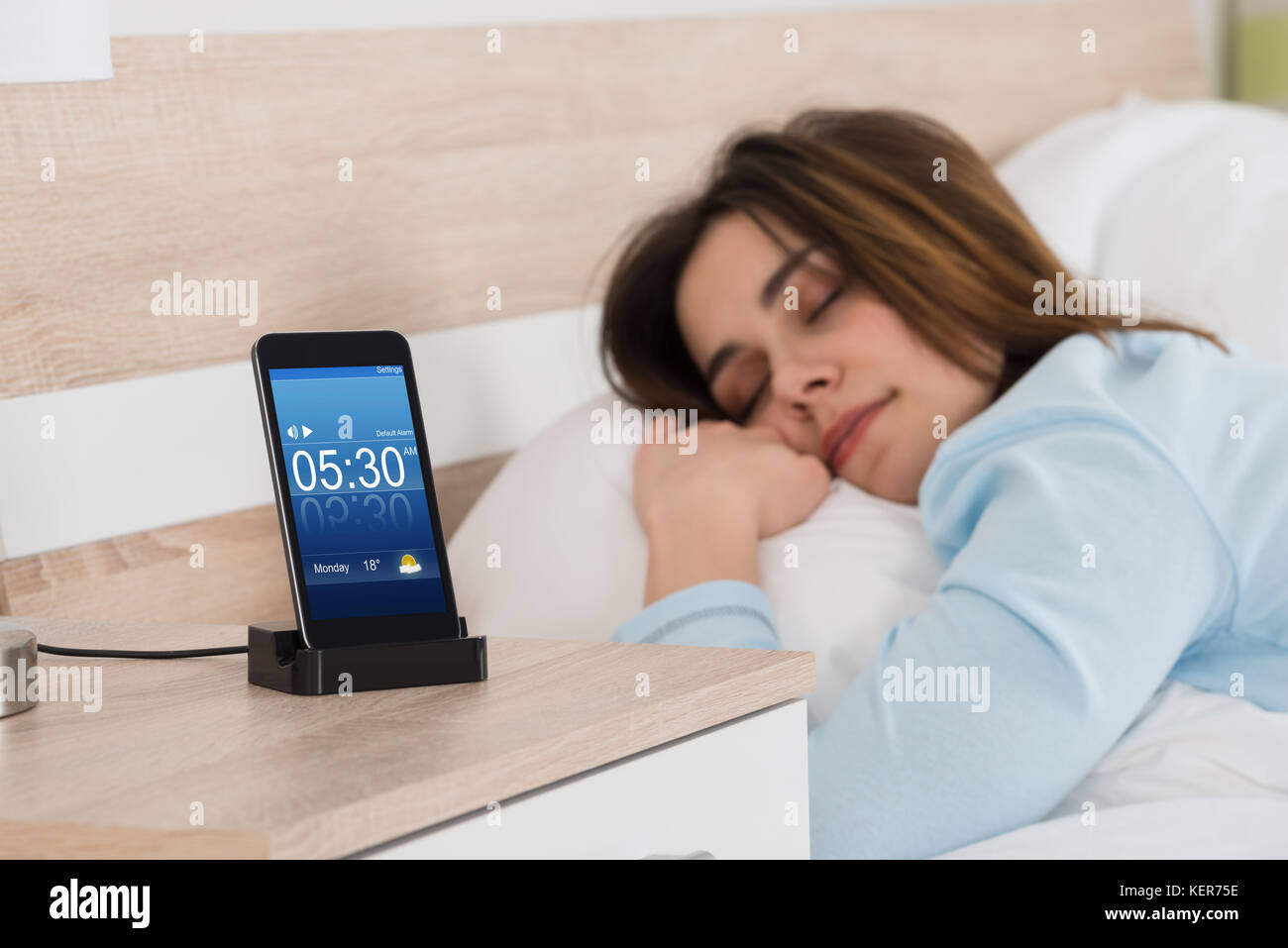 Young Woman Sleeping On Bed With Alarm On Mobile Phone Stock Photo