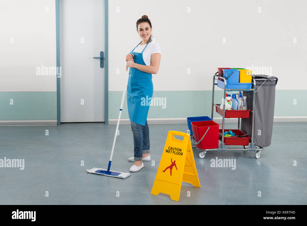 Female Janitor Mopping Corridor With Caution Sign Stock Photo
