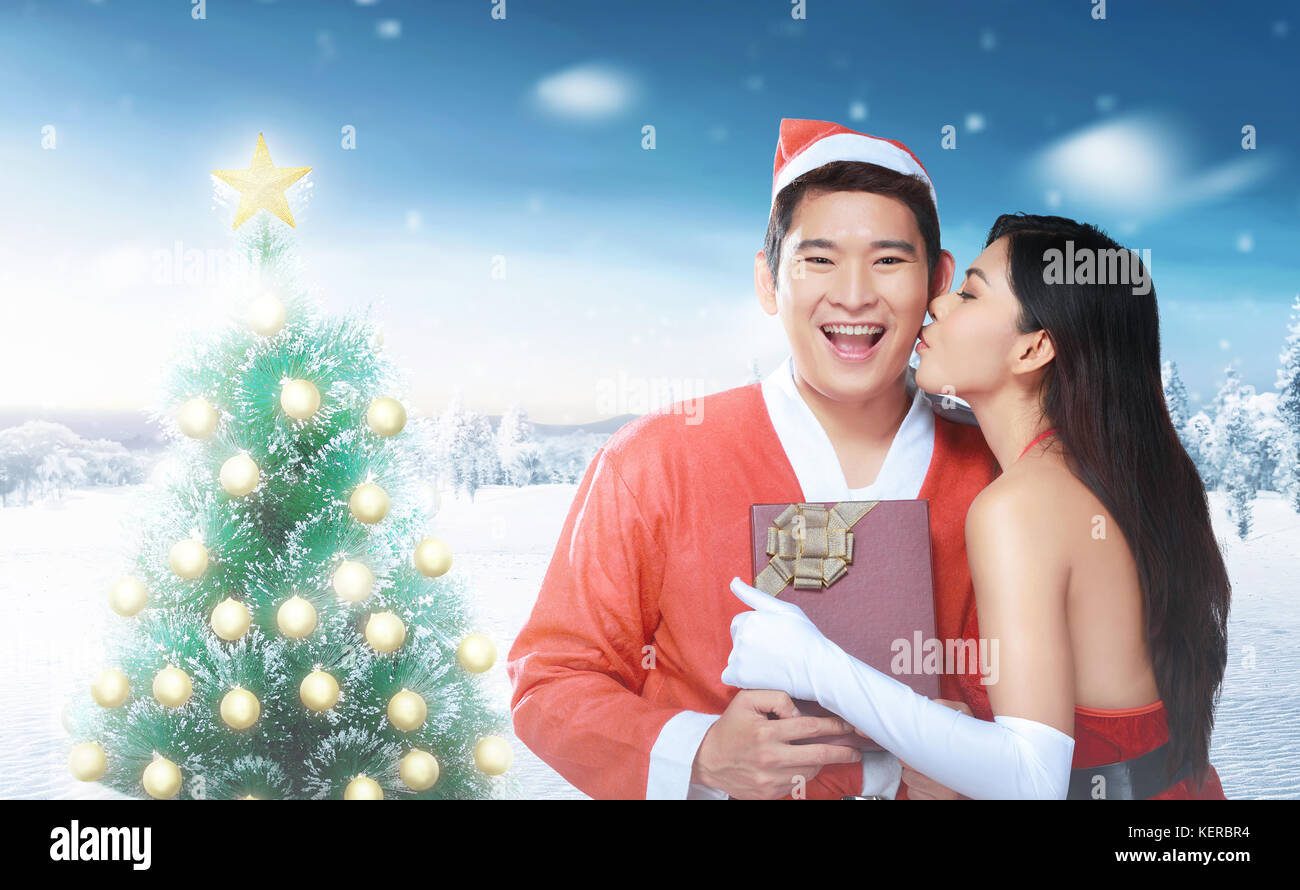 Romantic asian girl giving xmas gift and kissing her boyfriend at christmas Stock Photo