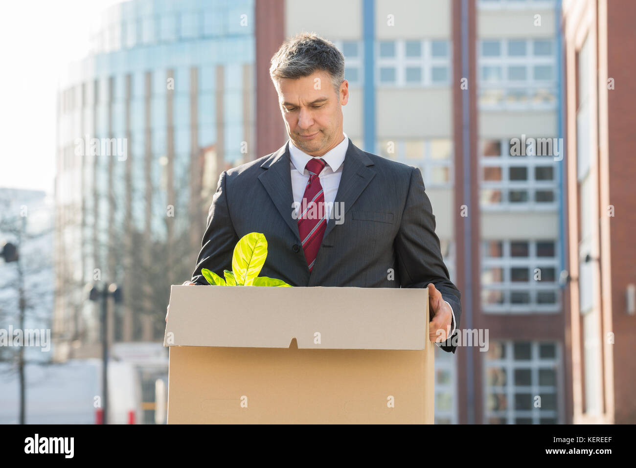 Disappointed Businessman Standing With Cardboard Box Outside Office