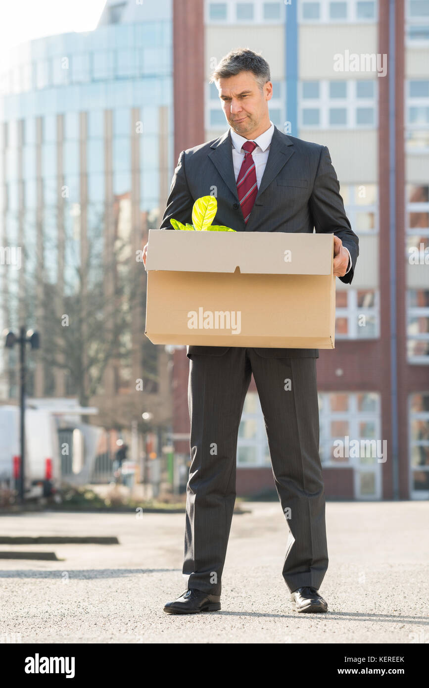 Disappointed Businessman Standing With Cardboard Box Outside Office