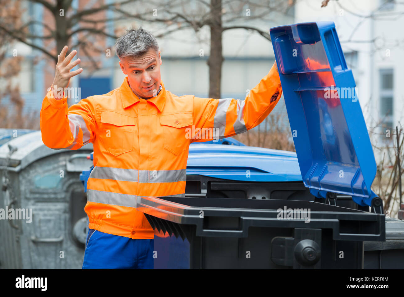 Unhappy Male Street Cleaner Looking In Dustbin Stock Photo