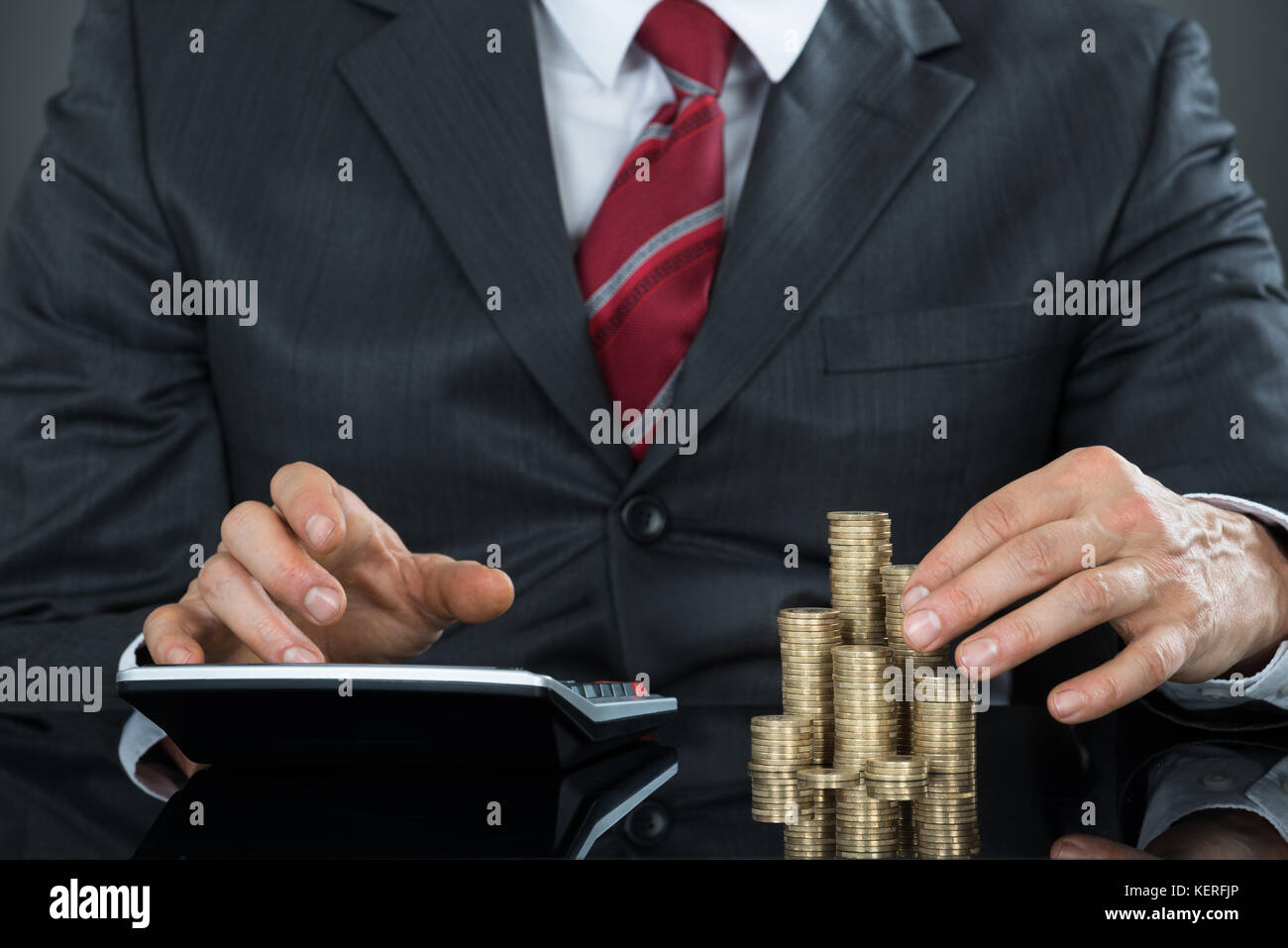 Close-up Of A Businessman Hand Counting Coins Using Calculator Stock Photo
