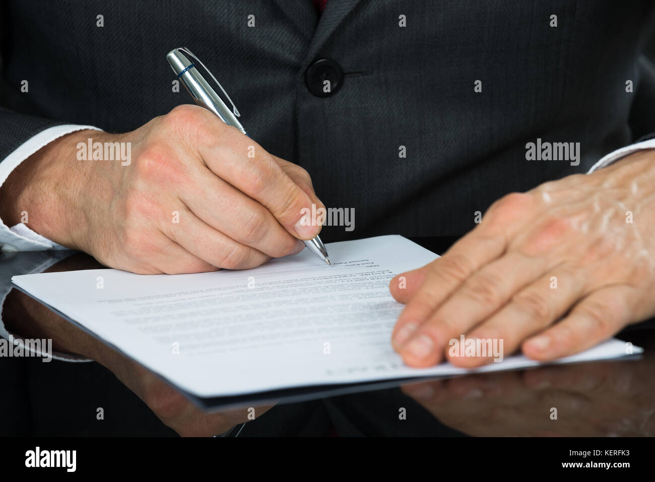 Close-up Of Businessman Hand Holding Pen Over Contract Form On Desk Stock Photo