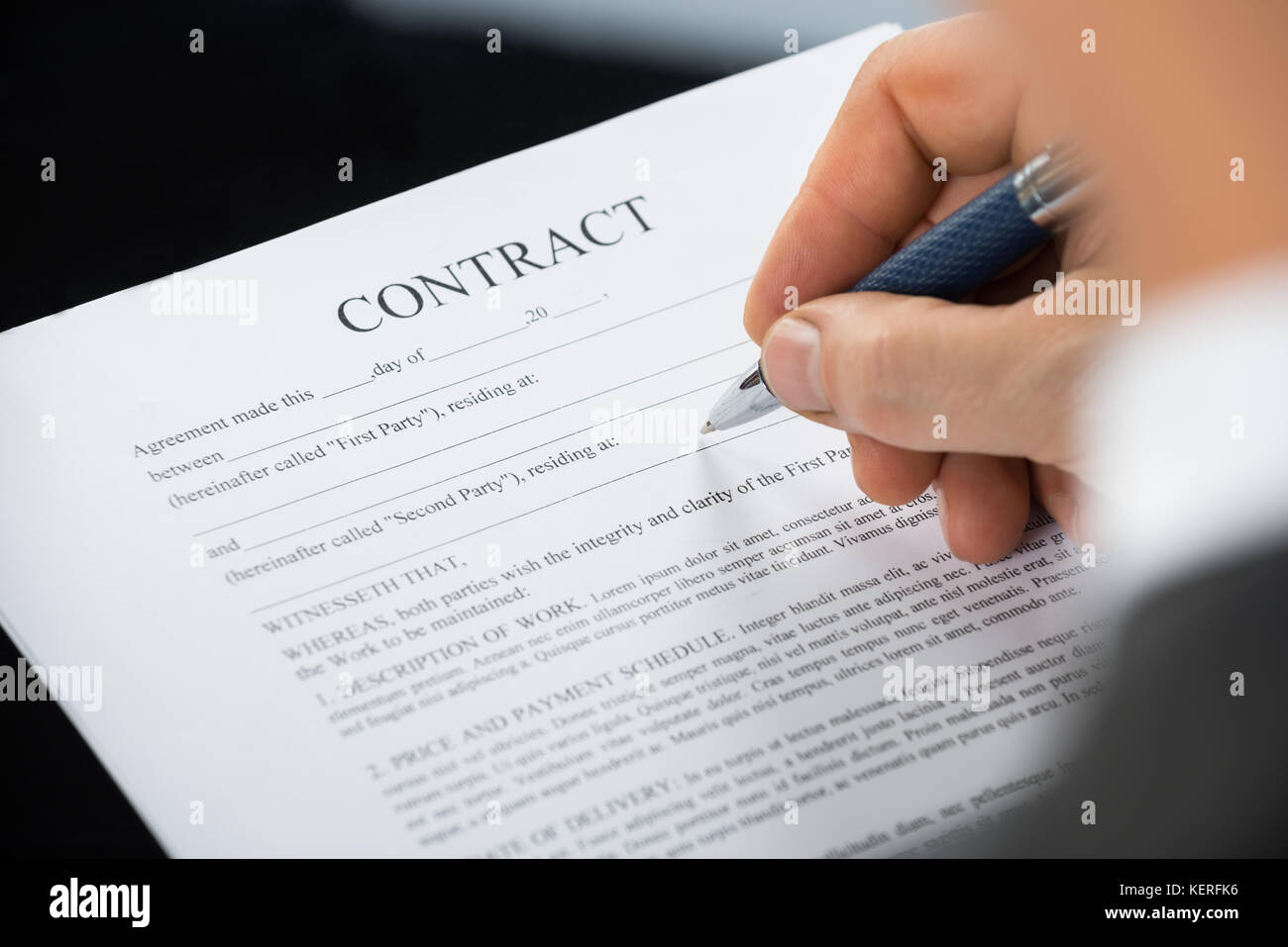 Close-up Of Businessman Hand Holding Pen Over Contract Form On Desk Stock Photo