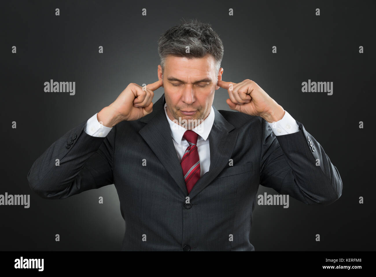 Portrait Of Mature Businessman With Eyes Closed And Fingers In His Ears Stock Photo