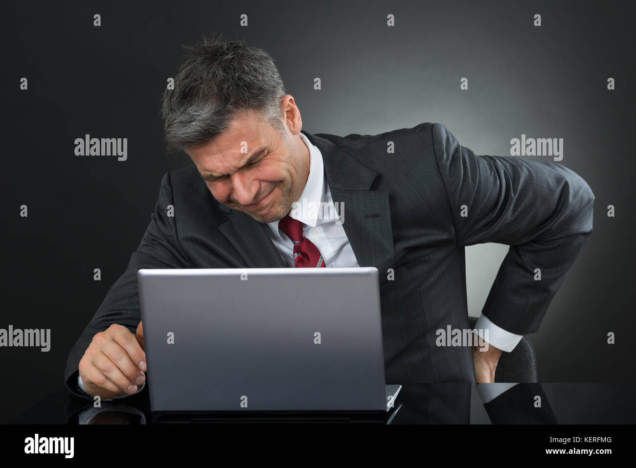 Mature Businessman Suffering From Back Pain While Working On Laptop At Desk Stock Photo