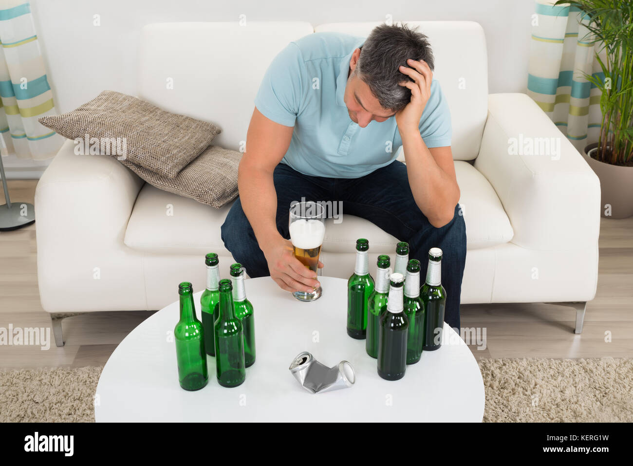 Mature Man Sitting On Sofa In Front Of Bottle Of Beer On Table Stock Photo